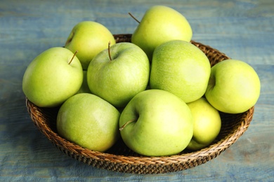 Photo of Wicker bowl of fresh ripe green apples on blue wooden table