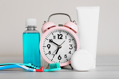 Composition with dental floss, alarm clock and different teeth care products on white wooden table