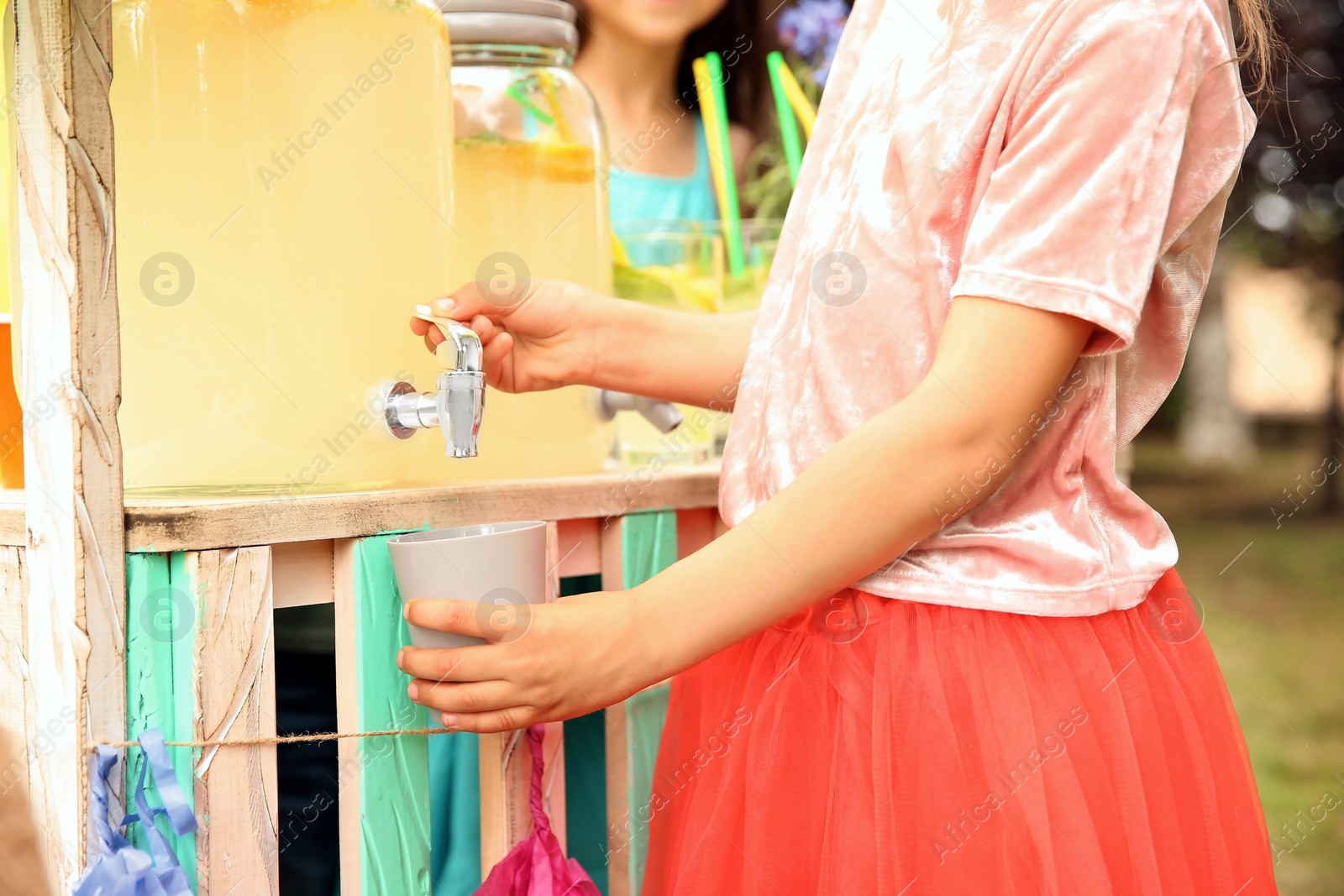 Photo of Little girl pouring natural lemonade into cup at stand outdoors