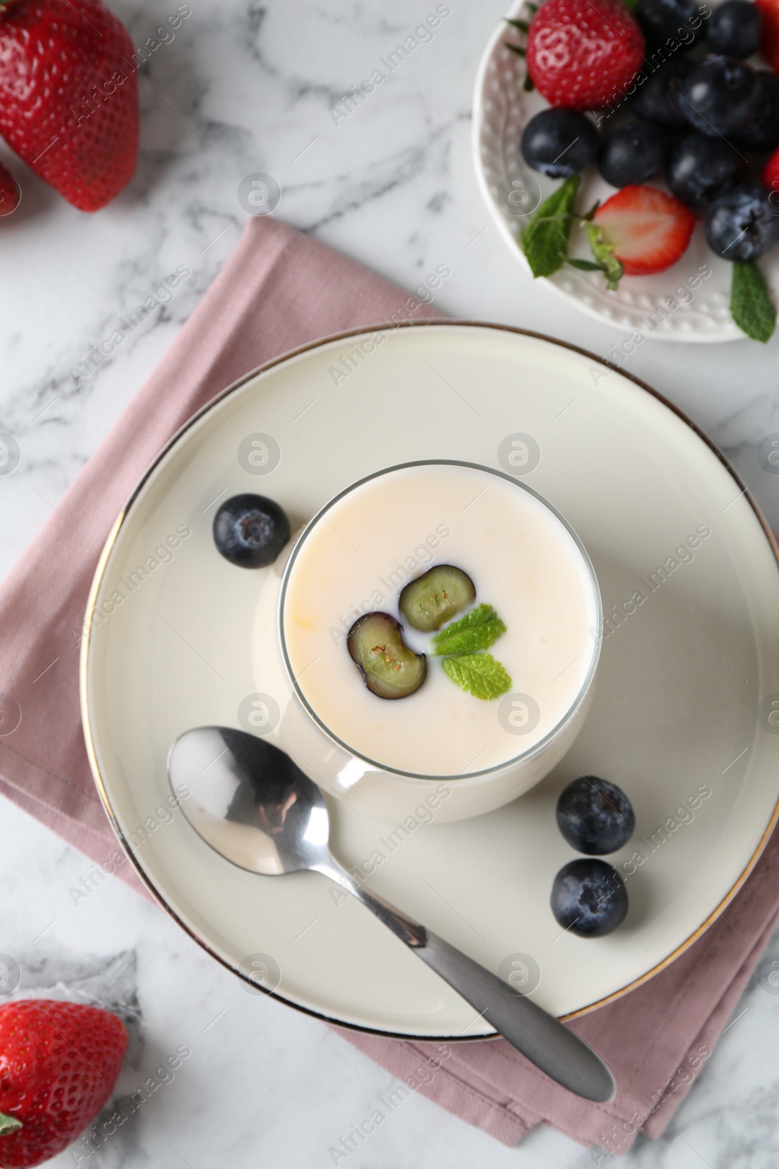 Photo of Tasty yogurt in glass and berries on white marble table, flat lay