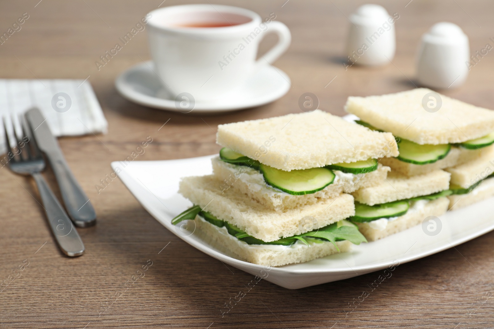 Photo of Plate with cucumber sandwiches served on wooden table. Space for text