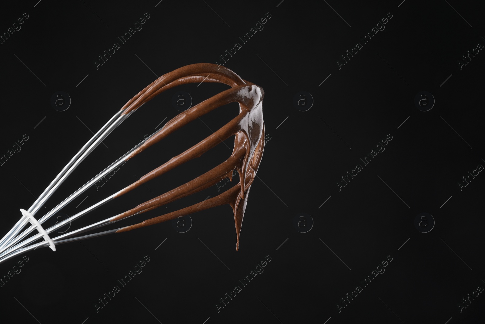 Photo of Chocolate cream flowing from whisk on black background, closeup. Space for text