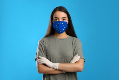 Woman wearing medical mask with European Union flag on light blue background. Coronavirus outbreak in Europe