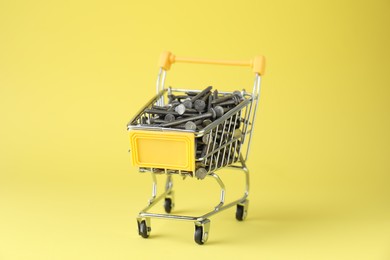 Metal nails in shopping cart on yellow background