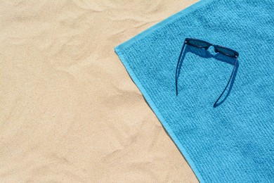 Photo of Towel and sunglasses on sand, top view with space for text. Beach accessories
