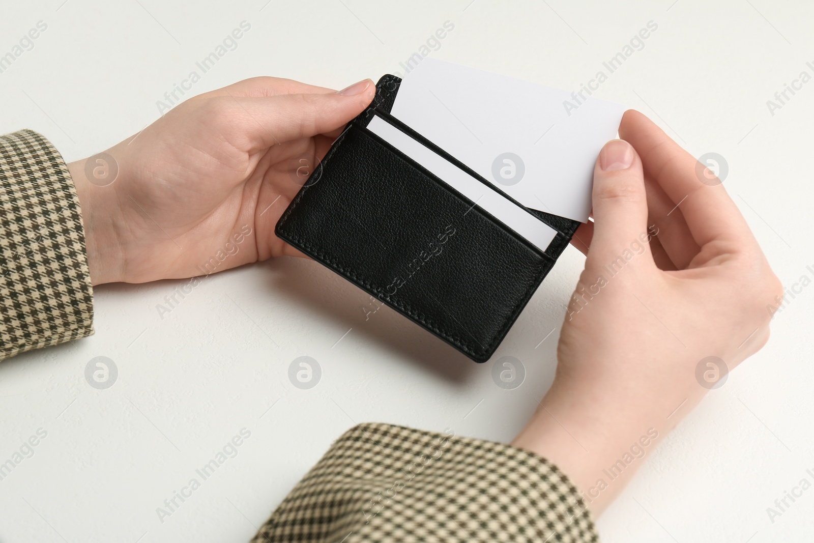 Photo of Woman holding leather business card holder with blank card at white table, closeup