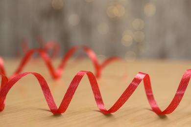 Photo of Shiny red serpentine streamer on wooden table against blurred lights, closeup