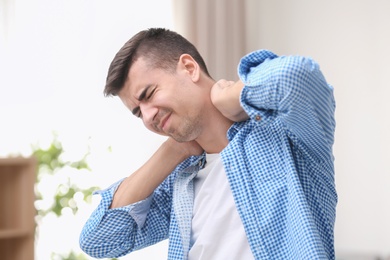 Photo of Young man suffering from neck pain at home