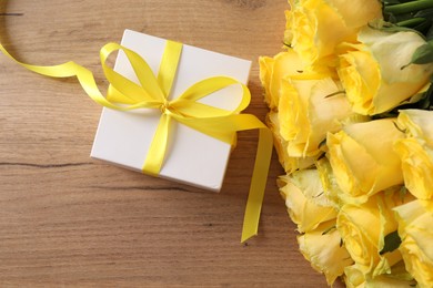 Beautiful bouquet of yellow roses and gift box on wooden table, flat lay