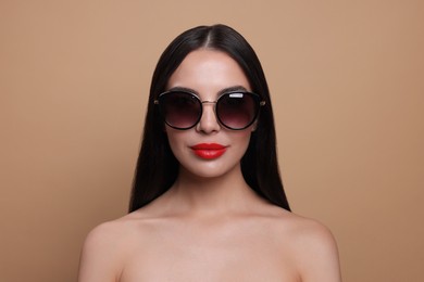Photo of Attractive woman in fashionable sunglasses against beige background