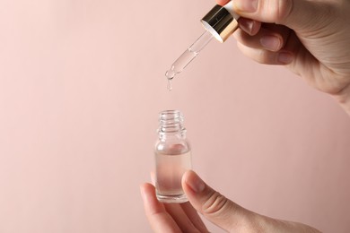 Photo of Woman dripping cosmetic serum from pipette into bottle on light pink background, closeup. Space for text