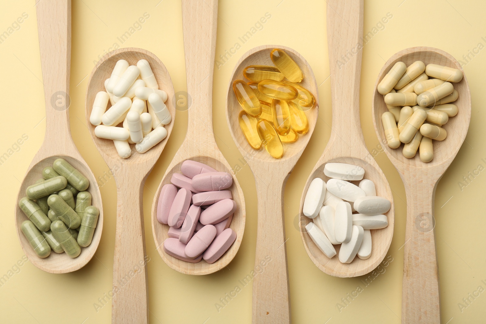 Photo of Different vitamin pills in spoons on pale yellow background, flat lay