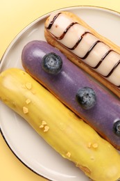 Delicious eclairs covered with glaze on yellow background, top view