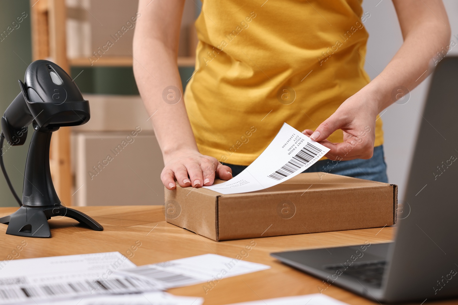 Photo of Parcel packing. Post office worker sticking barcode on box at wooden table indoors, closeup