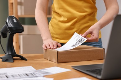 Parcel packing. Post office worker sticking barcode on box at wooden table indoors, closeup