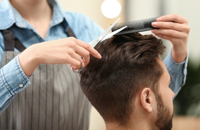 Photo of Barber making stylish haircut with professional scissors in beauty salon, closeup