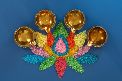 Diwali celebration. Diya lamps and colorful rangoli on blue background, flat lay