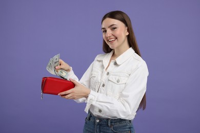 Happy woman putting money into wallet on purple background