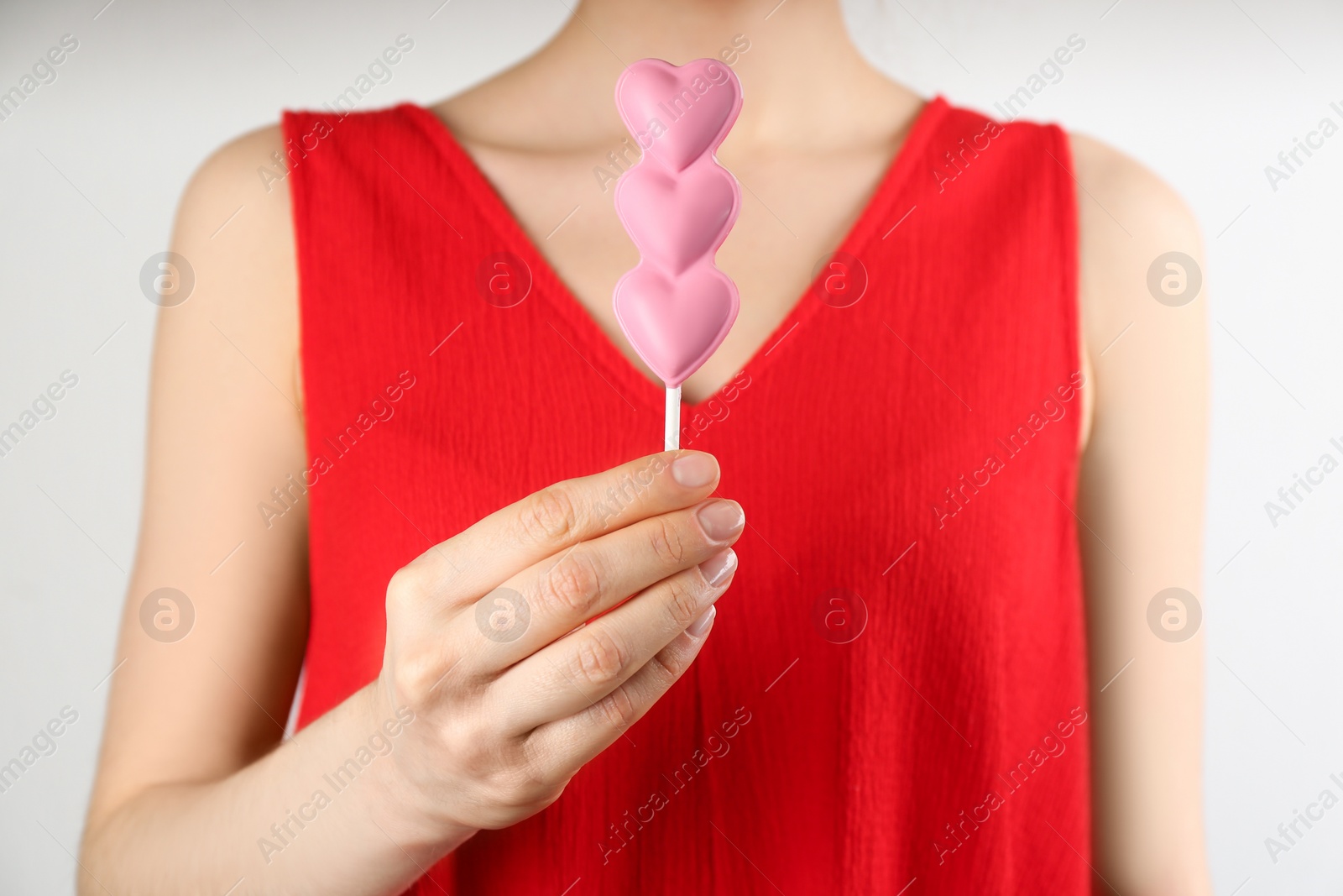 Photo of Woman holding heart shaped lollipop made of chocolate on light grey background, closeup