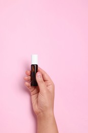 Woman with bottle of essential oil on pink background, closeup. Space for text