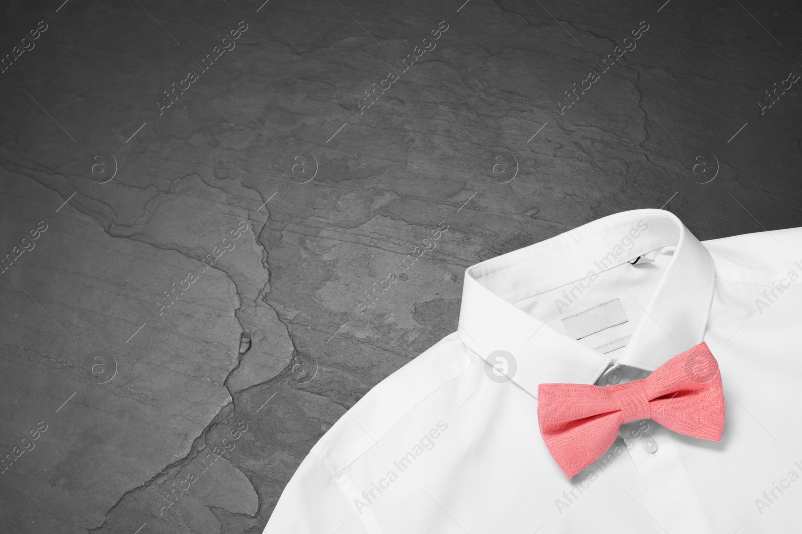 Photo of White shirt with stylish coral bow tie on grey background, top view. Space for text