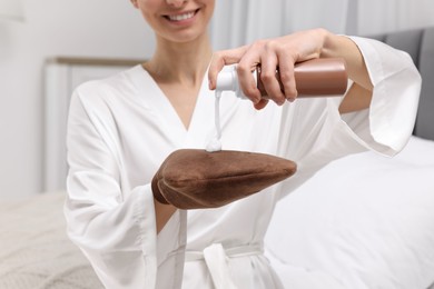 Photo of Self-tanning. Woman applying cosmetic product onto tanning mitt in bedroom, closeup