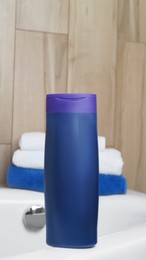 Photo of Purple bottle of bubble bath and towels on tub indoors