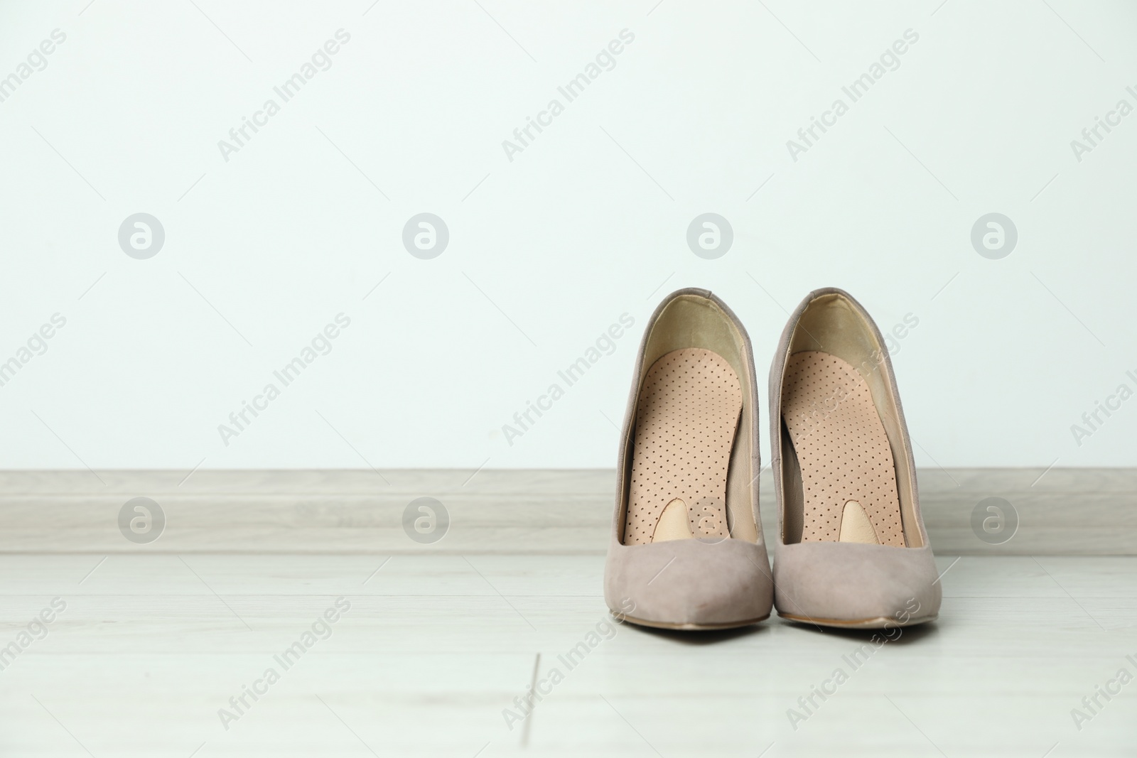 Photo of Orthopedic insoles in high heel shoes on floor. Space for text