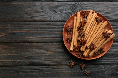 Photo of Aromatic cinnamon sticks and anise on black wooden table, flat lay. Space for text