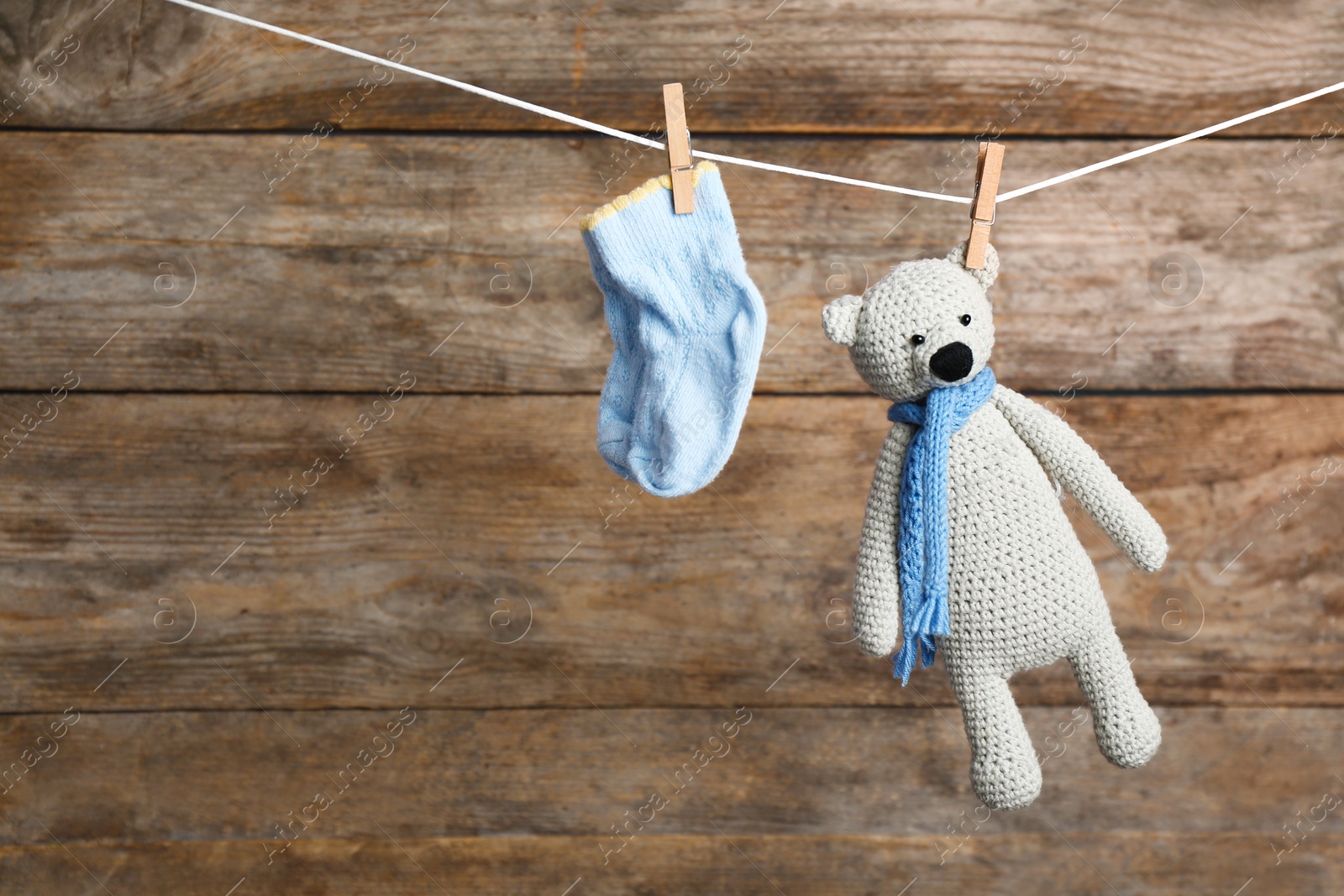 Photo of Pair of socks and toy bear on laundry line against wooden background, space for text. Baby accessories