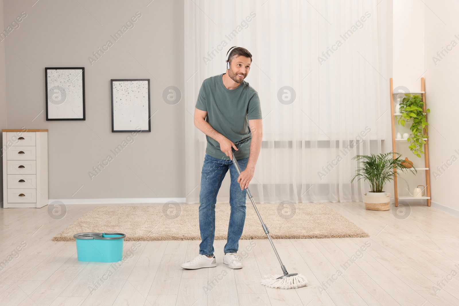 Photo of Enjoying cleaning. Man in headphones listening to music and mopping floor at home