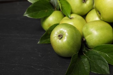 Photo of Ripe green apples with leaves on dark grey table, closeup. Space for text