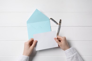 Photo of Woman with blank card at white wooden table, top view. Space for text