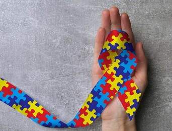 Image of World Autism Awareness Day. Woman with colorful puzzle ribbon on grey stone background, top view