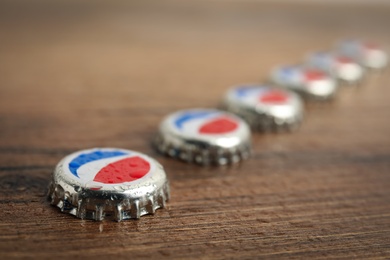 Photo of MYKOLAIV, UKRAINE - FEBRUARY 11, 2021: Pepsi lids with water drops on wooden background, closeup