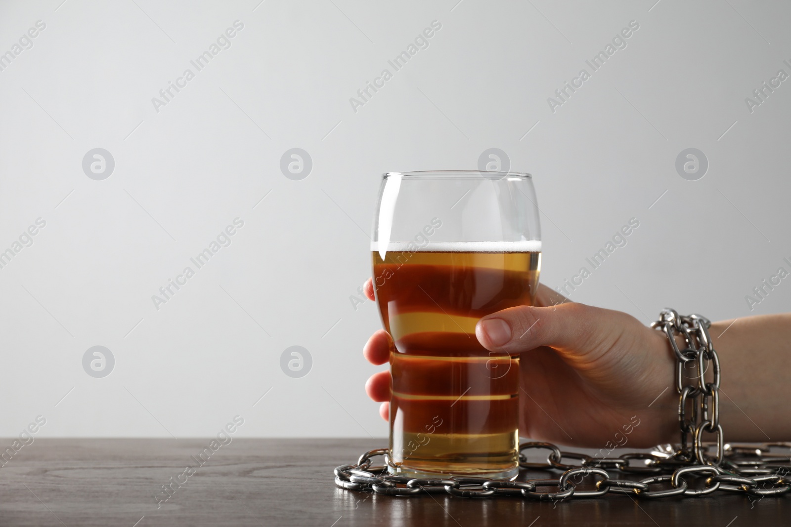 Photo of Woman with chained hand and glass of beer at wooden table against white background, closeup. Alcohol addiction