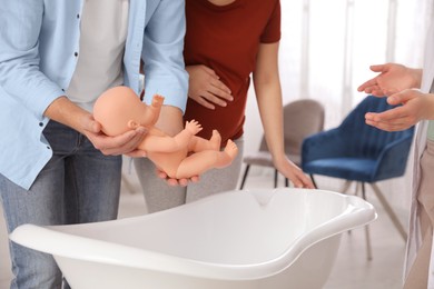Photo of Man with pregnant wife learning how to bathe baby at courses for expectant parents indoors, closeup
