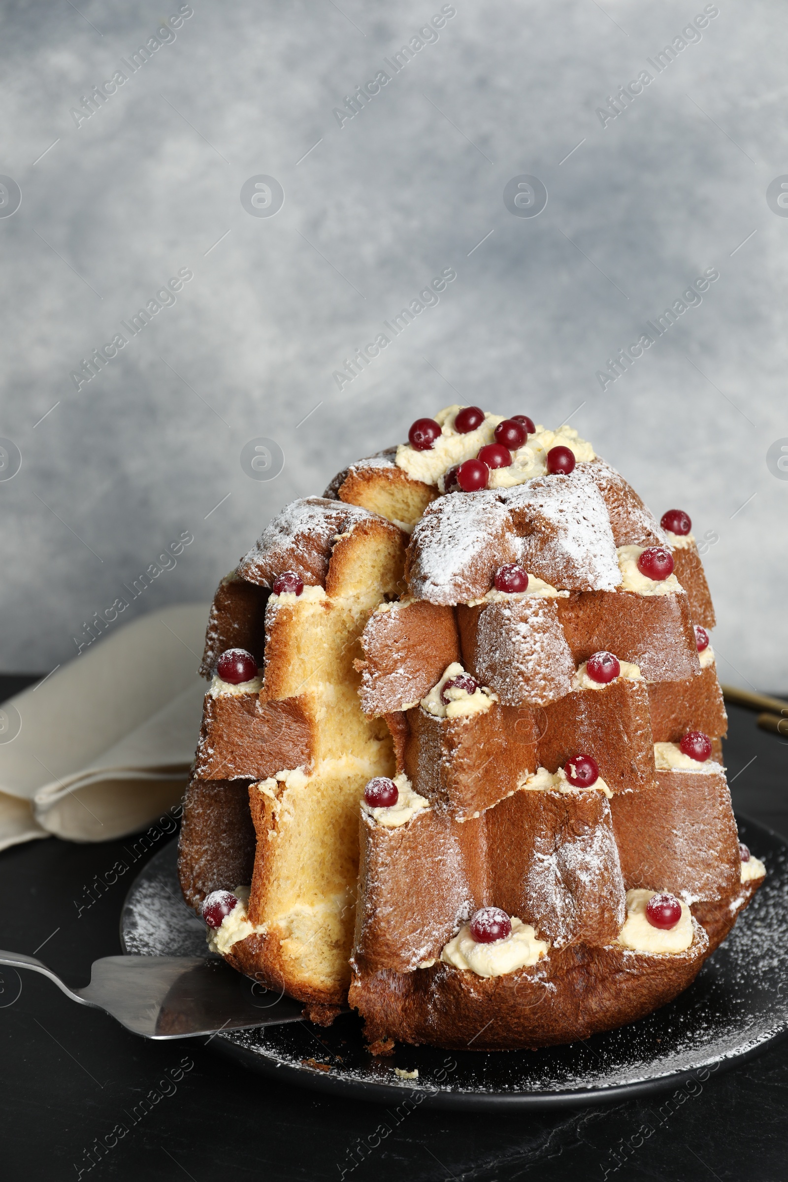 Photo of Taking slice of delicious Pandoro Christmas tree cake with powdered sugar and berries on black table
