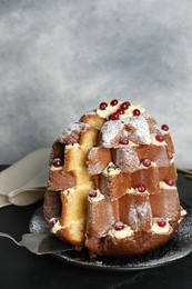 Taking slice of delicious Pandoro Christmas tree cake with powdered sugar and berries on black table