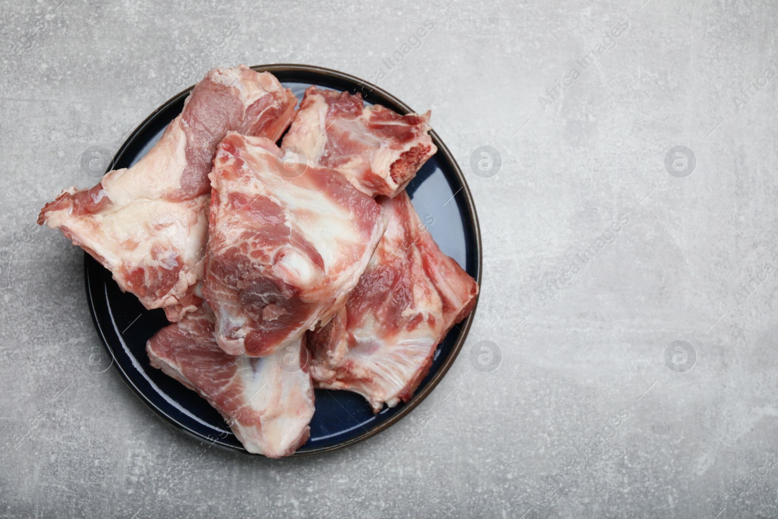 Photo of Plate with raw chopped meaty bones on grey table, top view. Space for text