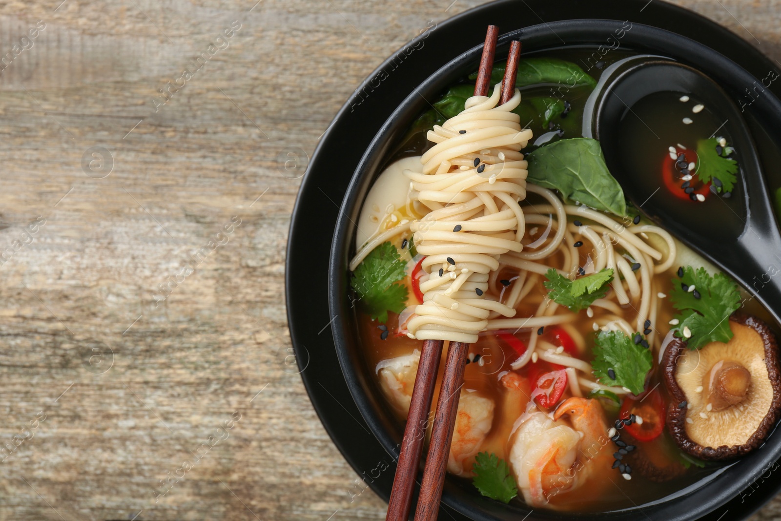 Photo of Delicious ramen with chopsticks and spoon in bowl on wooden table, top view with space for text. Noodle soup