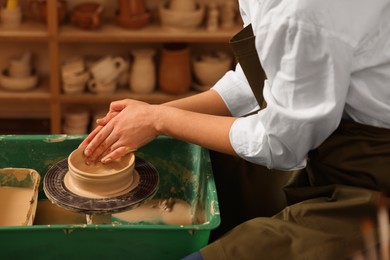 Photo of Clay crafting. Woman making bowl on potter's wheel in workshop, closeup