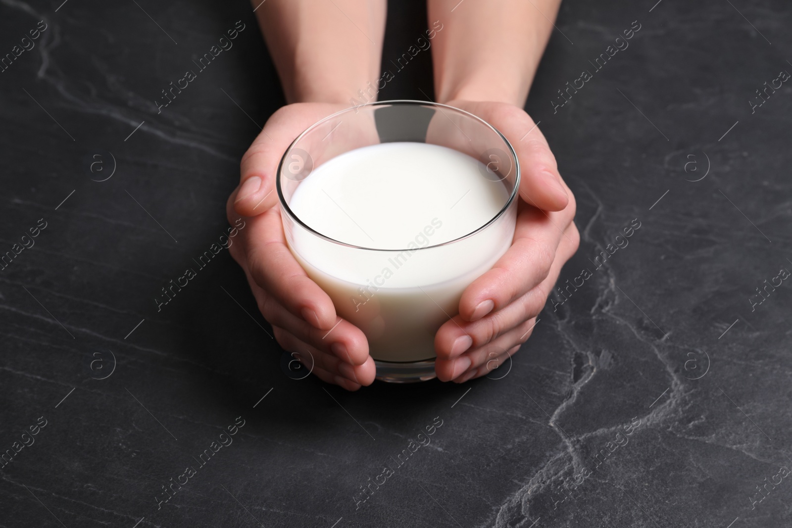 Photo of Woman holding glass of milk at black table, closeup