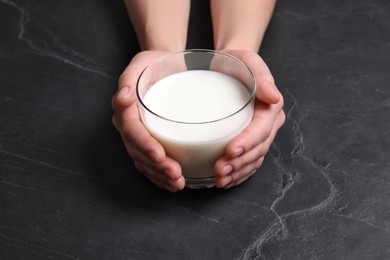 Photo of Woman holding glass of milk at black table, closeup