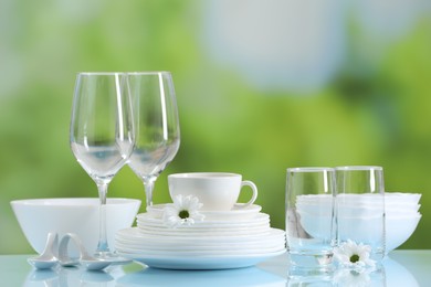 Set of many clean dishware and glasses on light blue table against blurred green background