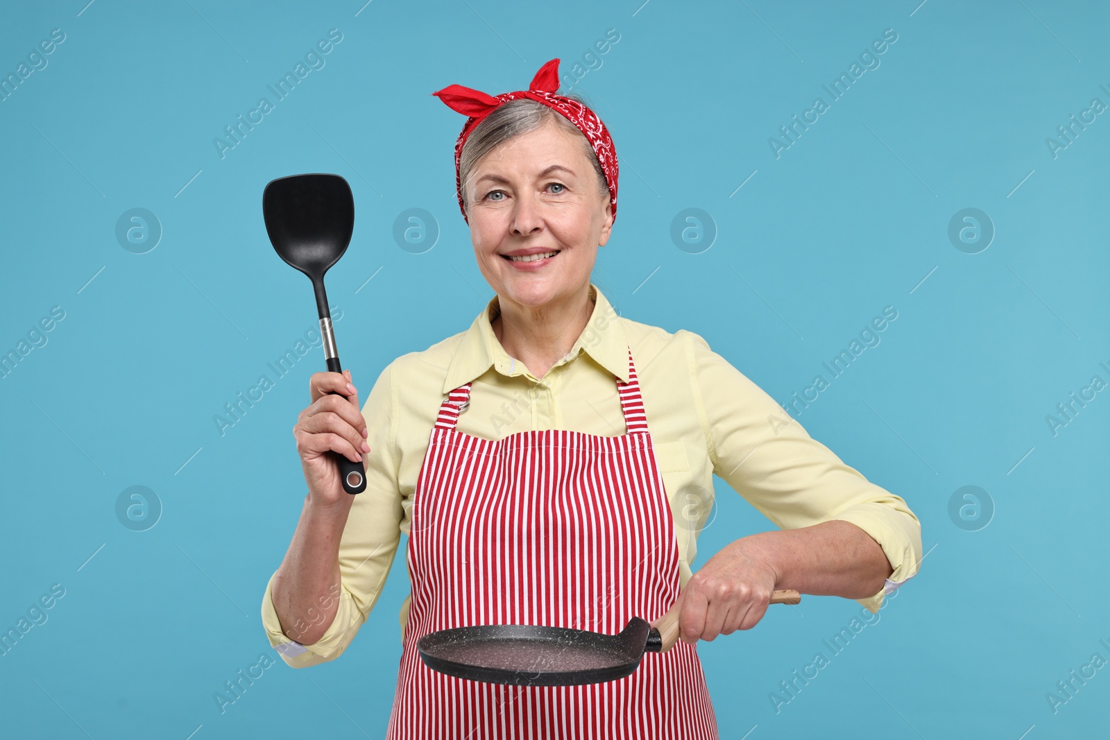 Photo of Happy housewife with turner and frying pan on light blue background