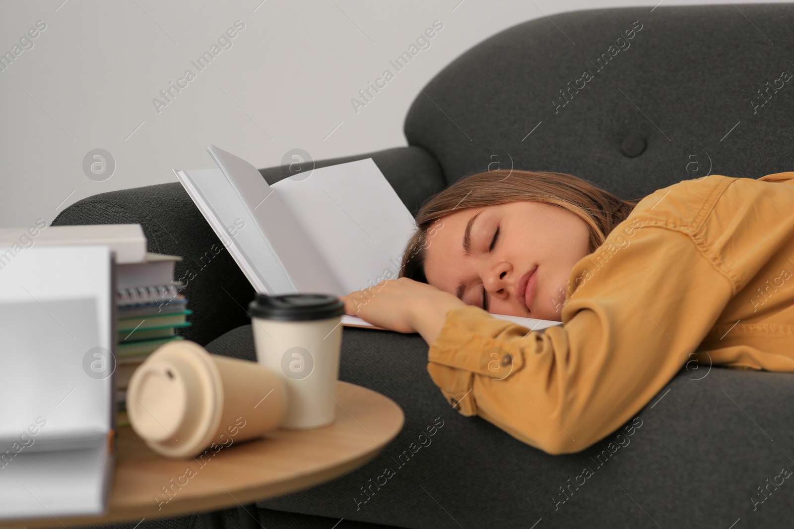 Photo of Young tired woman sleeping near books on couch indoors