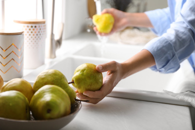 Woman holding fresh ripe pear in kitchen, closeup