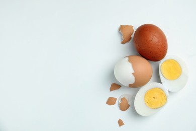 Hard boiled eggs and pieces of shell on white background, flat lay. Space for text