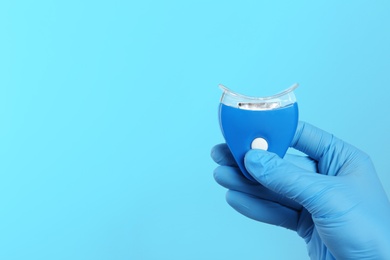 Photo of Dentist holding teeth whitening device on color background, space for text